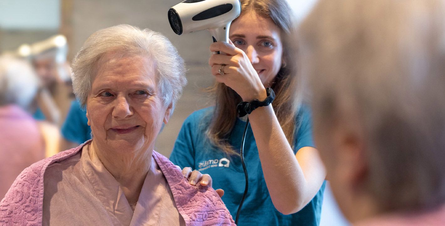 une aide à domicile sèche les cheveux d'une femme âgée