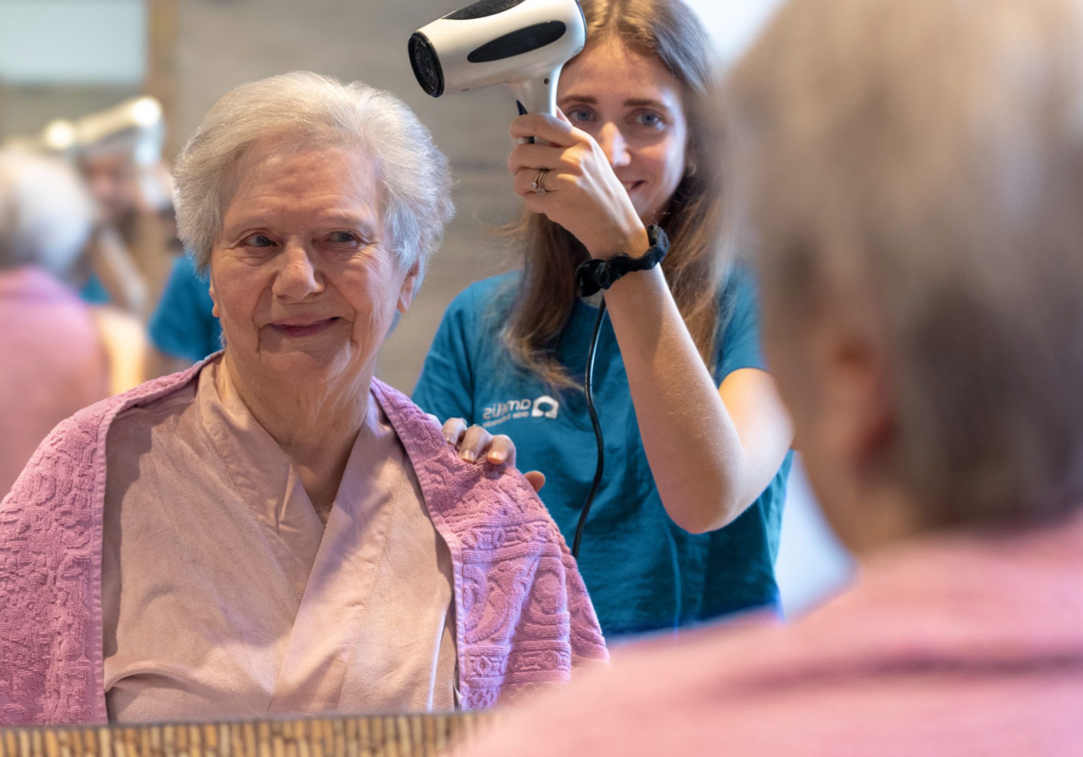 Une auxiliaire de vie sèche les cheveux d'une dame âgée