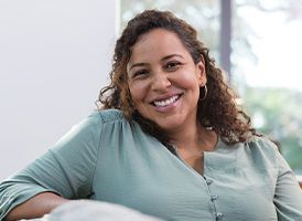 Femme d'une quarantaine d'année assise sur son canapé et souriante