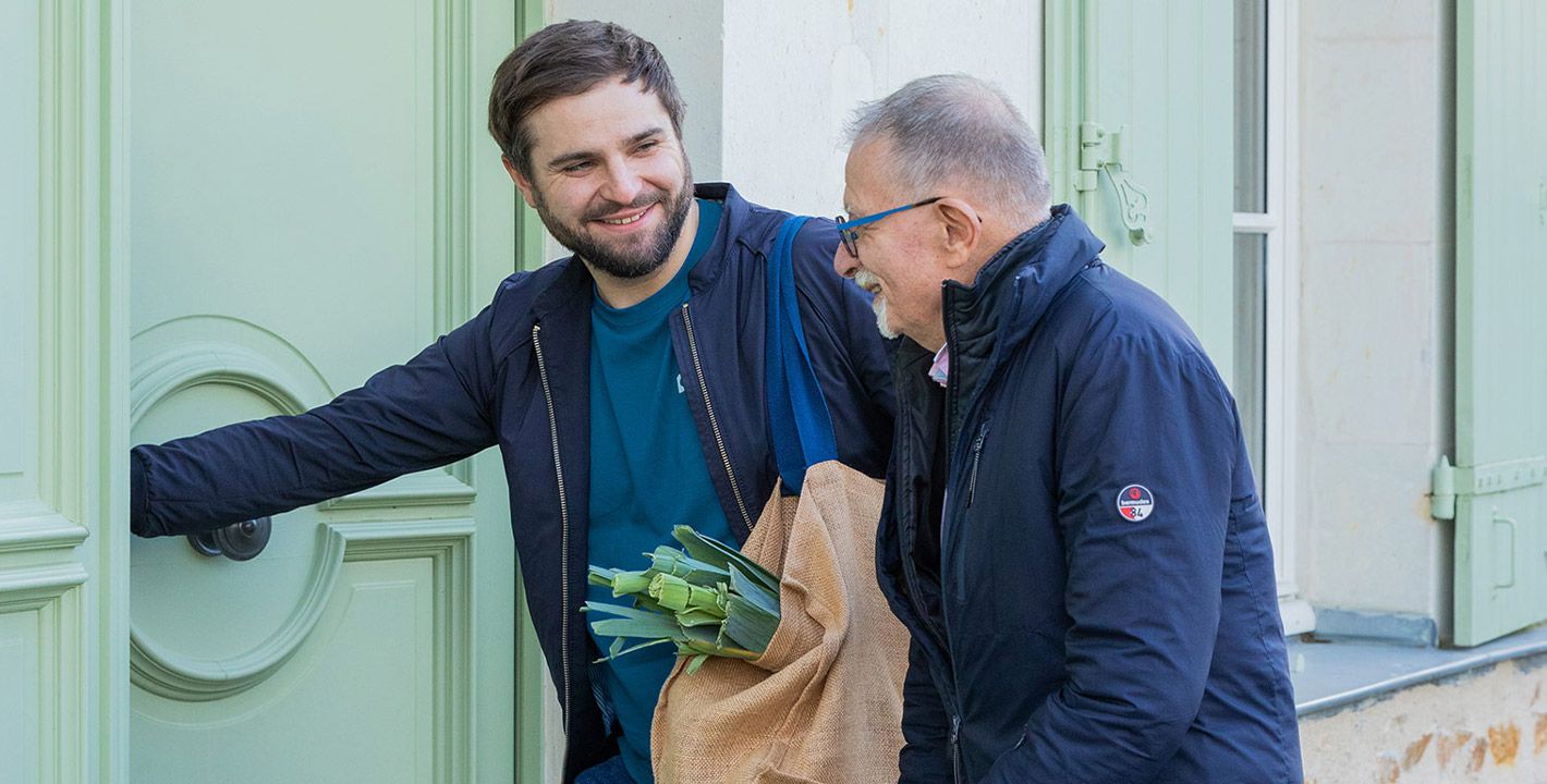 Un aide à domicile porte les courses d'un homme âgé