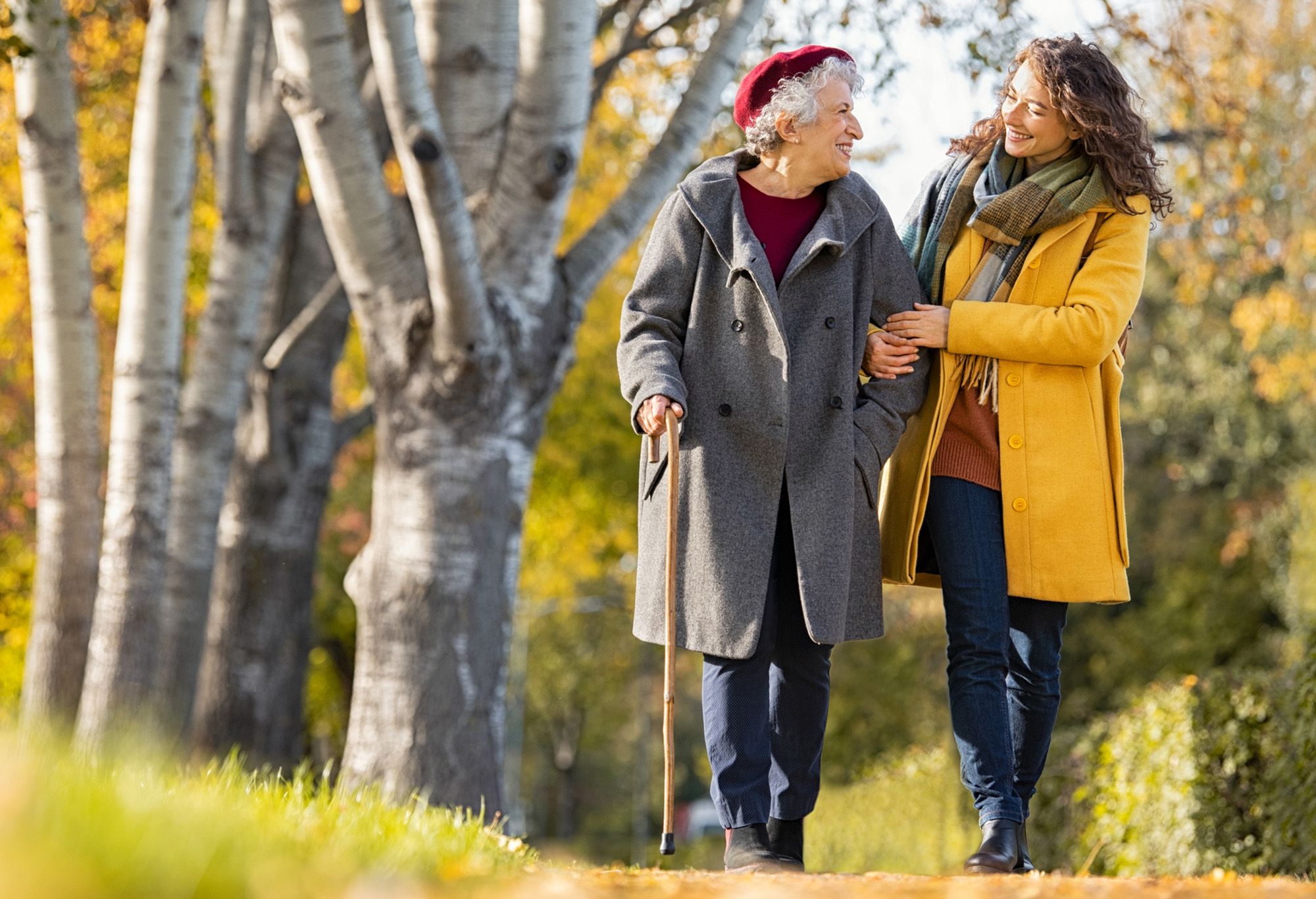 Une aide à domicile qui se promène avec une vieille femme qui marche avec une canne