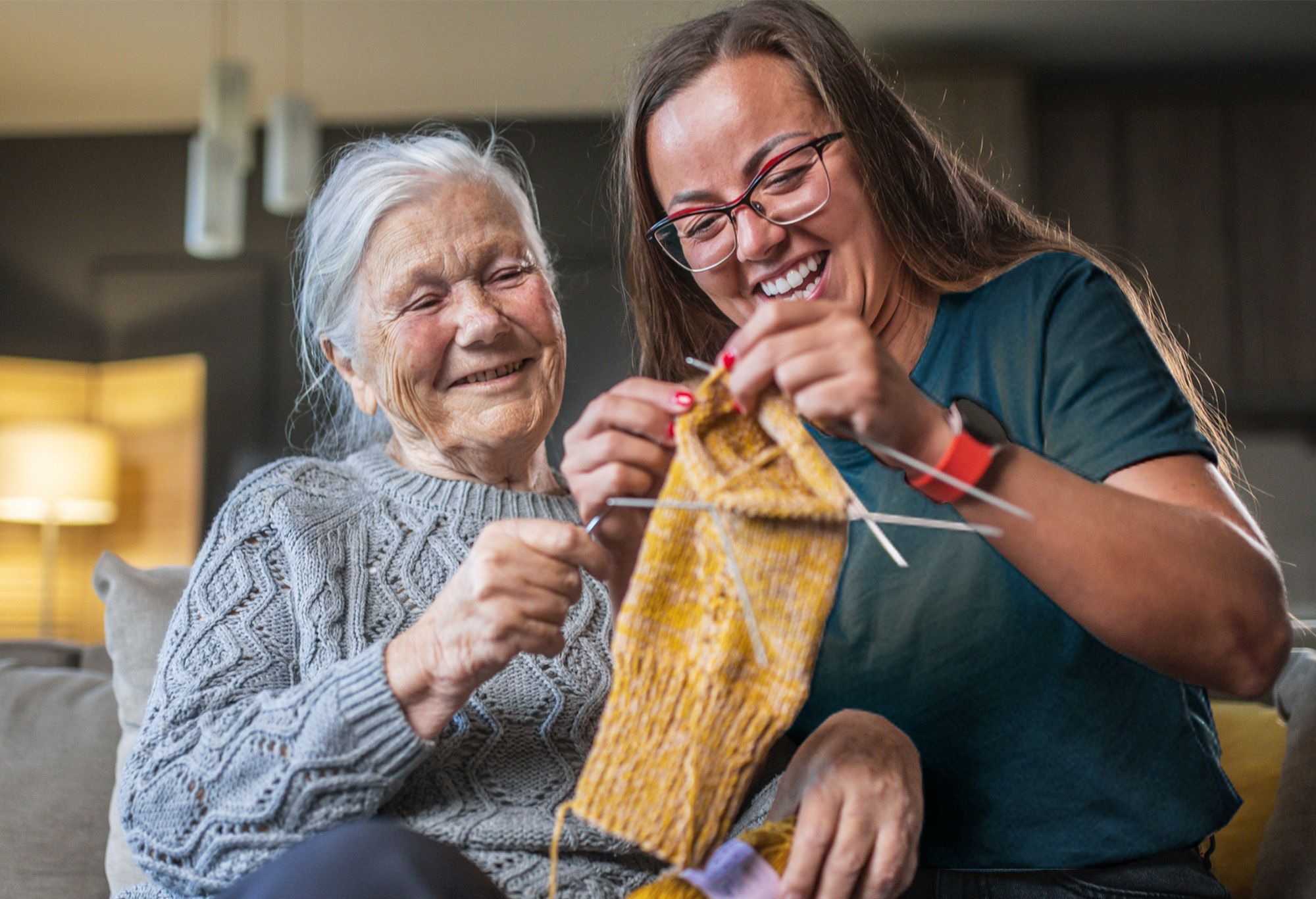 Aide à domicile qui fait du tricot avec une vieille femme sur un canapé