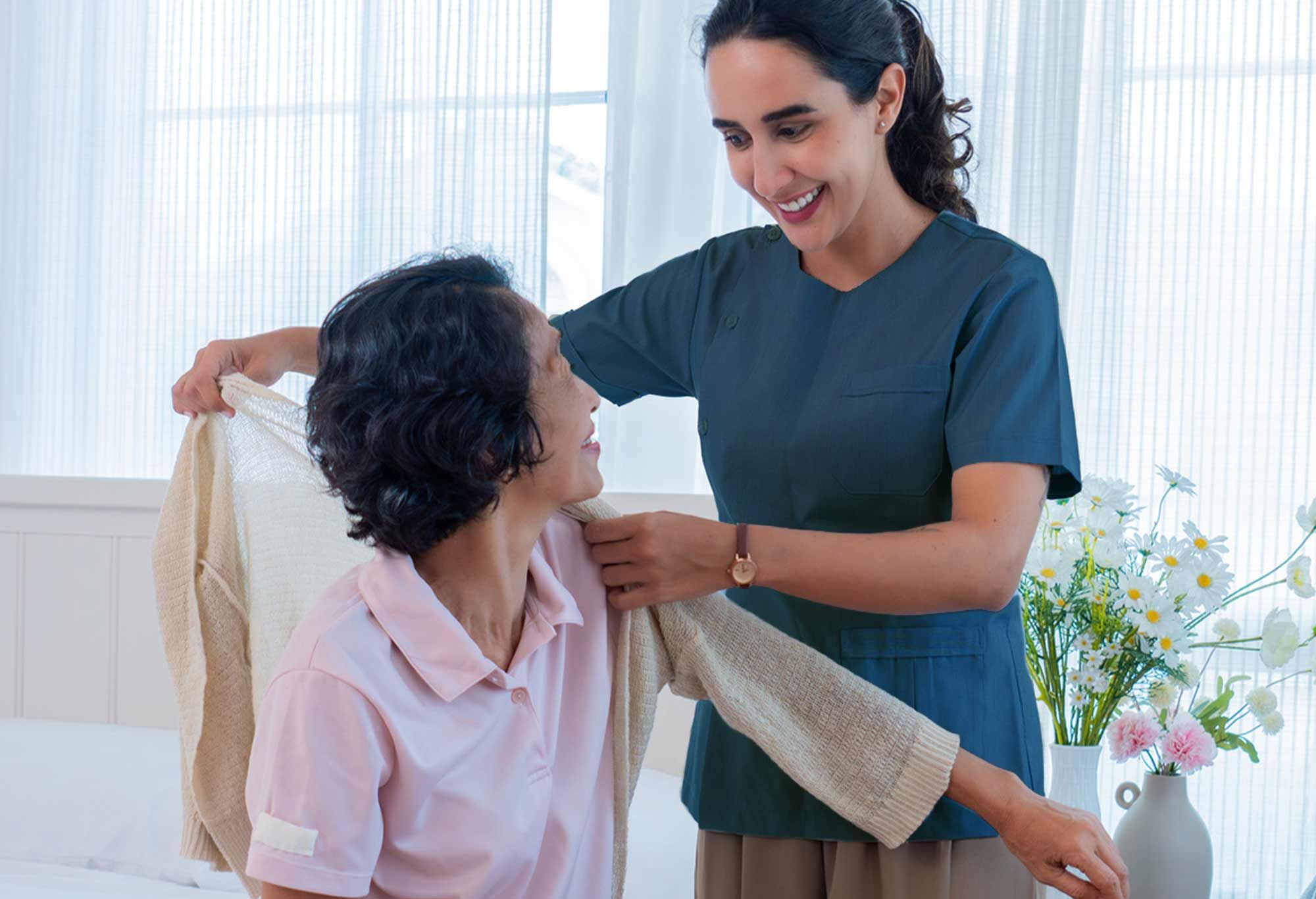 Aide à domicile qui habille une vieille femme