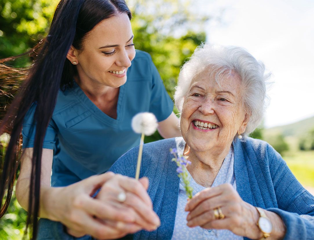 Une dame âgée tient une fleur dans sa main et son aide à domicile lui tient la main