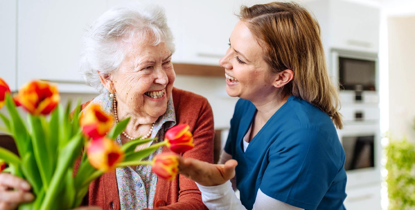 une femme âgée tient des fleurs avec son aide à domicile qui lui sourit